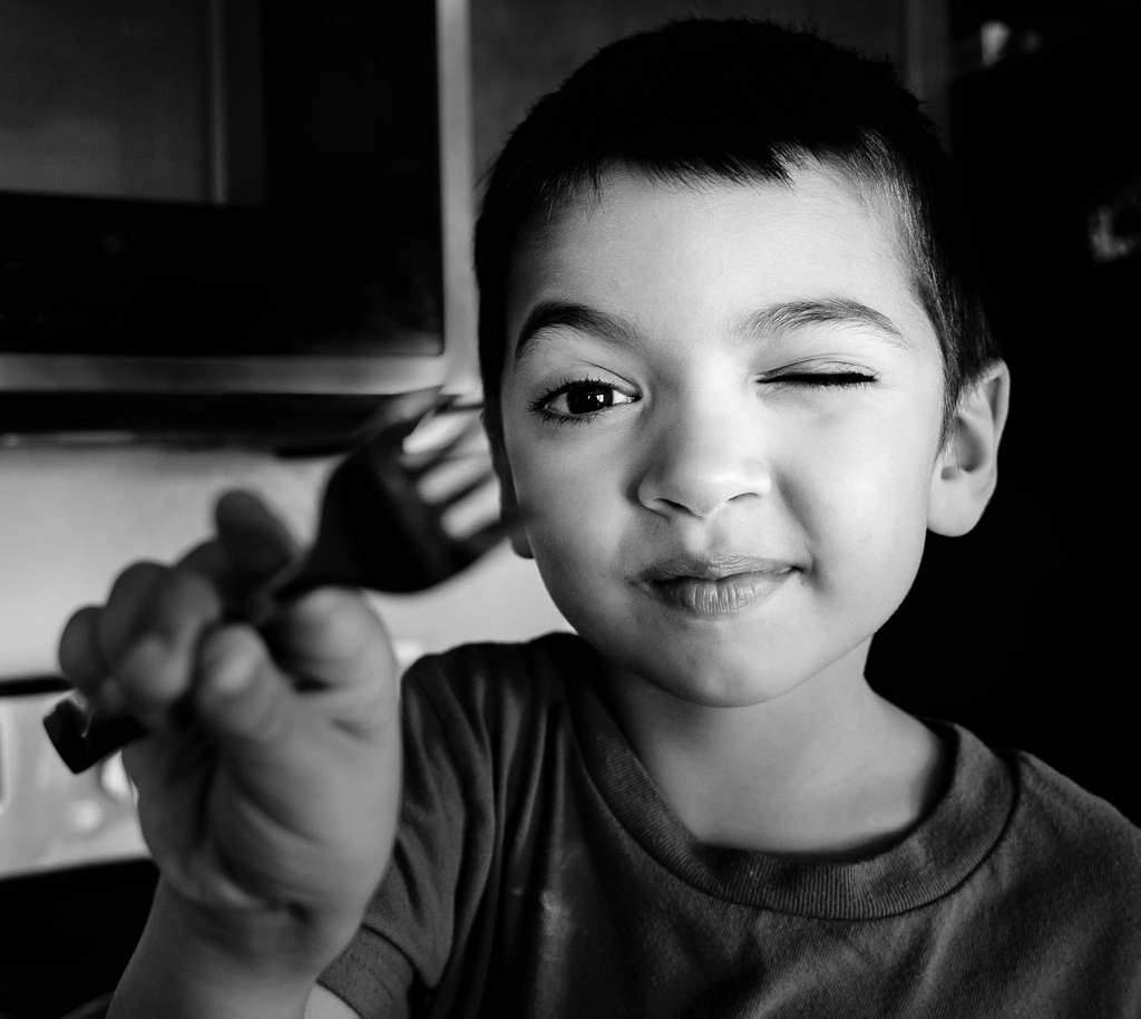 Un enfant pointe une fourchette vers l'objectif de l'appareil photo en faisant un clin d'œil.